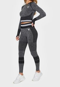 Šedá sportovní souprava obsahující top s dlouhým rukávem, který má přiléhavý střih a žebrované detaily, doplněná legínami s texturovanými vzory a pruhy.