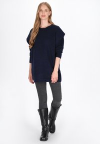 Granatowy sweter dzianinowy z przerośniętym designem ramion, sparowany z szarymi wąskimi dżinsami i czarnymi kozakami za kolano. Gładka faktura z luźnym krojem.
