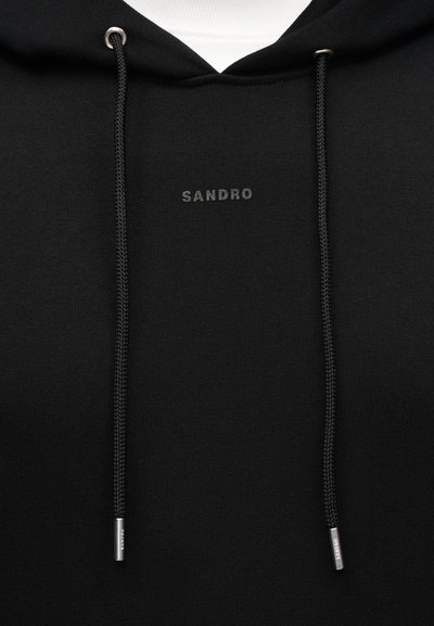 Μαύρο φούτερ με κουκούλα με το λογότυπο "SANDRO" σε μικρό γκρι κείμενο στο στήθος, διαθέτοντας μαύρα κορδόνια με ασημένιες μεταλλικές άκρες και λευκό ύφασμα ορατό στο εσωτερικό της κουκούλας.