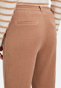 Lichtbruine corduroy broek met ribbeltextuur, twee achterzakken en een rechte snit, gedragen met een crème gestreepte trui.