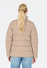 Beige puffjakke med vandret syninger, høj krave og elastiske manchetter. Bæres med lyseblå jeans, der fremhæver et afslappet look.