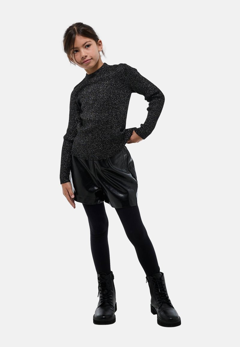 Haut noir à manches longues avec un éclat métallique, associé à un short en simili cuir noir. Des leggings noirs et des bottes à lacets complètent l'ensemble.