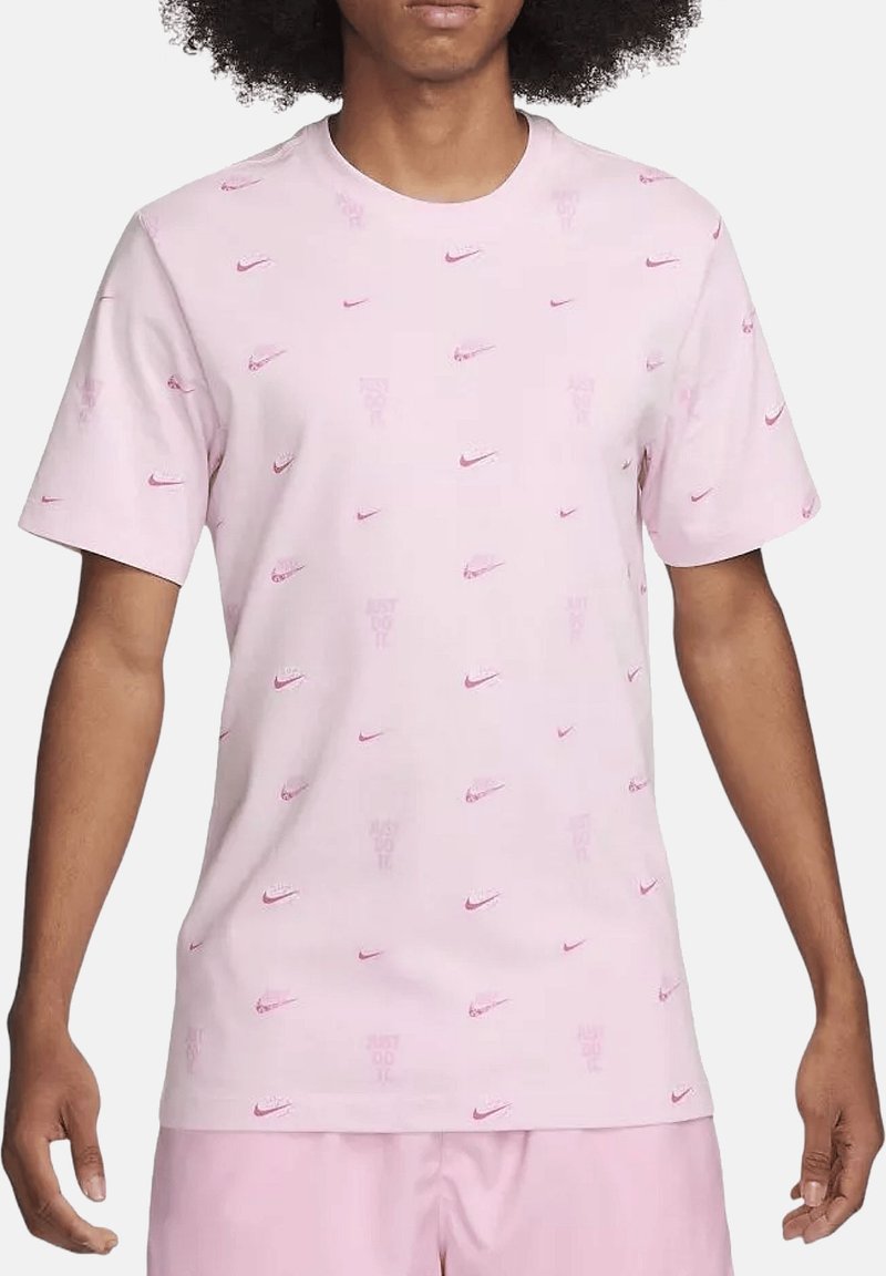 T-shirt rose à manches courtes en coton, avec un motif subtil de logo Nike répété et le texte "Just Do It" en rose plus foncé.