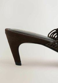 Brun ruskind sandal med mellemhøj hæl, flettet remdetalje og spids tå, vist fra siden på en lys baggrund.