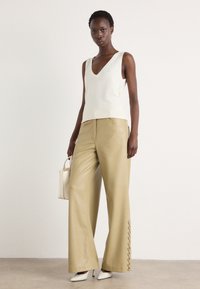 Débardeur en tricot crème avec un profond col en V, associé à un pantalon large en simili cuir beige avec des accents de lacets à l'ourlet. Talons blancs et sac à main.