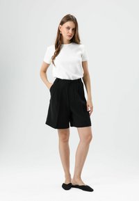 Witte T-shirt met korte mouwen, zwarte geplooide shorts met hoge taille en zwarte ballerina's. Rechte snit, zachte textuur, minimalistisch ontwerp.