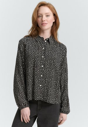 Schwarzes Button-Up-Hemd mit weißem abstraktem Punktmuster, langen Ärmeln und abgerundetem Saum. Hergestellt aus leichtem Stoff mit lockerer Passform.