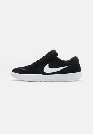 Zwarte suède sneakers met witte accenten, met een ronde neus, dikke witte zool en zwarte veters. Opvallend wit Nike-logo aan de zijkant.