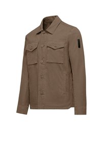 Giacca in tela khaki con colletto classico, due tasche sul petto e tasche laterali. Presenta una chiusura frontale con bottoni e una toppa sulla manica sinistra.