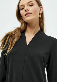 Sort, langærmet top med V-hals, lavet af glat stof. Model bærer gyldne dråbeøreringe. Enkel og minimalistisk design.