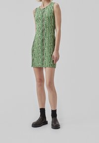 Robe sans manches verte avec un motif texturé vertical, associée à des chaussettes noires à la cheville et des chaussures à enfiler sombres.