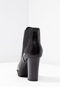 Botín de cuero negro con tacón, paneles laterales elásticos, perforaciones decorativas y un acabado suave. Tacón ancho para mayor estabilidad.