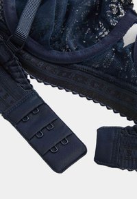 Navy Spitzen-BH mit Netzeinsätzen, verstellbaren Trägern und einer gewellten Kante. Mit einem Haken- und Ösenverschluss mit mehreren Einstellmöglichkeiten zur Anpassung der Passform.