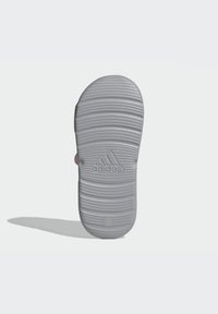 Suola di sandaletta in gomma grigia con un motivo rigato, caratterizzata dal logo Adidas impresso sulla superficie. Nessun segno visibile o dettagli aggiuntivi.