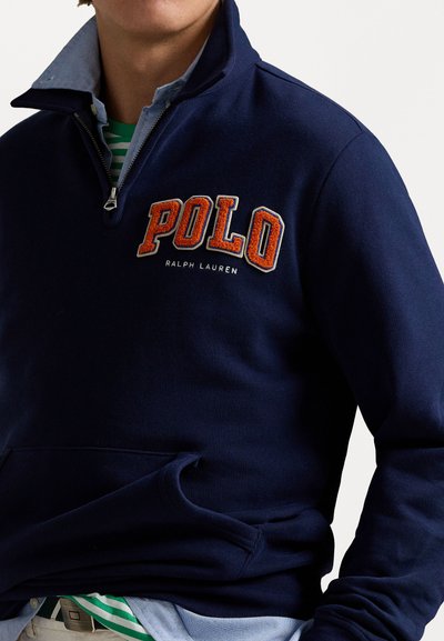 Sudadera de cuello alto en color navy con media cremallera, que presenta el logo bordado en naranja "POLO" y el texto "RALPH LAUREN". Tejido suave y texturizado.