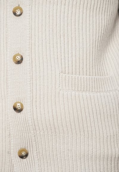 Krém színű kötött kardigán bordázott textúrával, öt nagy aranyszínű gombbal és egy kis elülső zsebbel.