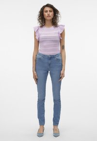 Lila pletena majica z nabranimi rokavi, ki ima vodoravne vzorce. V kombinaciji s svetlo modrimi skinny jeans hlačami in svetlo modrimi koničastimi petkami.