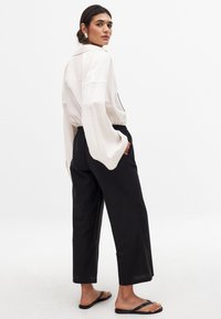 Losse crèmekleurige blouse met brede mouwen, zwarte elastische taillebroek en zwarte slippers. Gladde stof met een minimalistisch ontwerp.