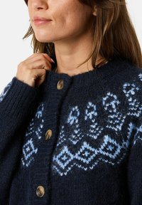 Marineblauwe gebreide cardigan met lichtblauwe geometrische patronen, ronde halslijn en vijf grote beige knopen aan de voorkant, gemaakt van textuurachtig wol.