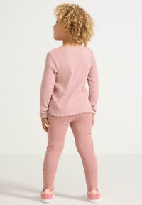 Vaaleanpunainen ribattua pitkähihaista puseroa, jossa on reikävalmiit helmassa, ja siihen sopivat legginsit, joissa on brodeerattuja kukkia. Kengät ovat vaaleanpunaiset valkoisella pohjalla ja logolla.