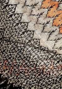 Textil med ett texturerat mönster i svarta, beiga och orange nyanser, med intrikata vävda mönster och en mjuk, lagerpålagd utseende.