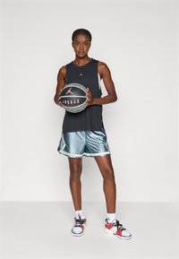 Svart ermeløs tanktop, slimete teal shorts med hvit kant, svart og rød basketball, og sporty sneakers med røde og hvite aksenter.