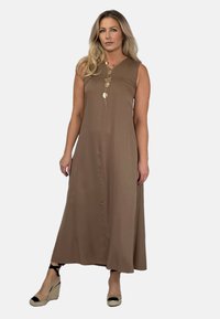 Brązowa, bezrękawna sukienka maxi o prostym kroju, z przodem z guzikami i gładką fakturą. Połączona z sandałami na koturnie.
