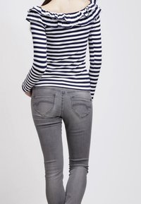 Gestreiftes Off-Shoulder-Top mit Rüschensaum, in Marineblau und Weiß. Eine graue Slim-Fit-Jeans mit Gesäßtaschen und Nähten.