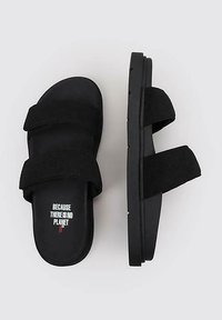 Sandalias negras con dos cintas anchas de textil, plantilla contorneada y suela de goma sólida. El texto en la plantilla dice "PORQUE NO HAY PLANETA".