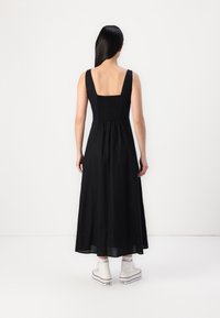 Rochie maxi neagră cu spate pătrat, bretele late, bust ajustat și fustă fluidă. Purtați cu adidași albi cu talpă înaltă. Textură netedă.