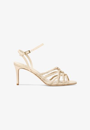 Beige hoger hak sandalen hebben gevlochten banden, een open teenontwerp, een verstelbare enkelgesp en een slanke stilettohak.