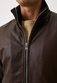 Bruine leren bomberjack met een zwarte ribbelkraag, zilveren ritsluiting en een gebreide textuur aan de binnenkant.