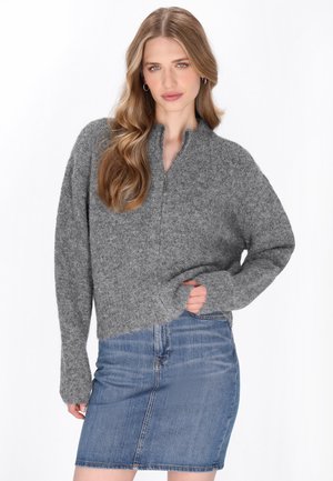 Pulover gri, texturat, cu guler cu fermoar la jumătate și croială lejeră, asortat cu o fustă din denim ajustată. Material moale cu mâneci lungi și formă relaxată.