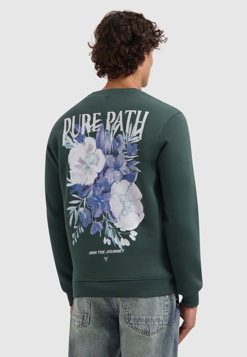 Groene sweatshirt met ronde hals, voorzien van een bloemenprint in blauw- en wittinten op de achterkant met de tekst "PURE PATH" erboven en "OWN THE JOURNEY" eronder.