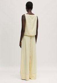 Gelbes, tailliertes Oberteil mit rechteckigem Ausschnitt und einer Rückennaht, kombiniert mit weiten, bodenlangen gelben Hosen aus leichtem Stoff.