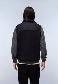 Svart pufferväst med gråa ullärmar, ribbade manschetter och en slät yta. Baksidan är helt svart med en matt finish.