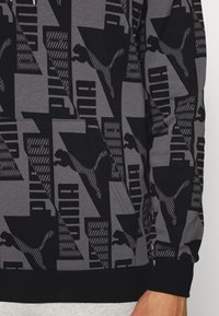 Sweat à capuche Puma avec un motif géométrique noir et gris, comprenant des logos et des graphismes stylisés, avec un ourlet et des poignets côtelés.