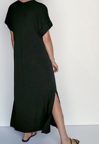 Mustapuku maxi-mekko lyhyillä käärityillä hihoilla, sivurei'ill�ä ja pehmeällä tekstuurilla, rento istuvuus ja polven korkeudelle ulottuva halkio.