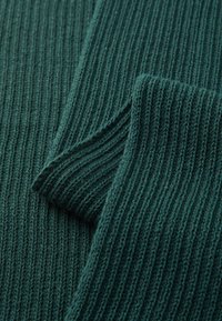 Dark green ribbed knit sweater fabric with a folded sleeve showing textured vertical lines and soft yarn fibers.
