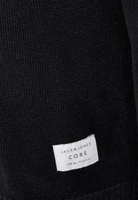 Czarna dzianina o gładkiej fakturze. Widoczna jest wszywka z napisem "JACK & JONES CORE" oraz numerem produktu.