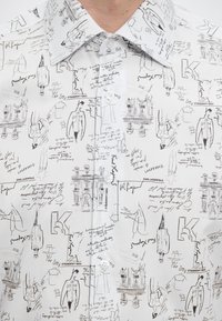 Weißes Hemd mit Knöpfen und schwarzem Skizzenprint von Gebäuden, Modefiguren, handgeschriebenem Text und dem wiederholten Namen Karl Lagerfeld.