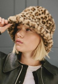 Leopard-print faux fur bucket hat with a wide brim and soft texture, paired with a black leather jacket and a white T-shirt.