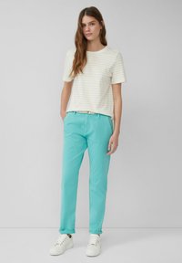 Licht gestreepte short-sleeve shirt in crème en beige gecombineerd met turquoise broeken en witte sneakers, met een relaxte pasvorm en opgerolde mouwen.