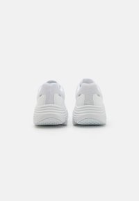 Białe sportowe buty z teksturowaną siateczką, wyściełanym kołnierzem i żłobioną gumową podeszwą, charakteryzujące się eleganckim, minimalistycznym designem.