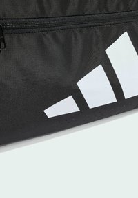 Čierna športová taška z textúrovaného materiálu s bielym geometrickým logom. Obsahuje zipsové zapínanie a malé perforované detaily.