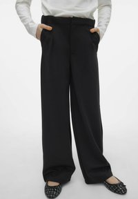 Szerokie czarne spodnie z zakładkami, wykonane z gładkiego materiału, z bocznymi kieszeniami i płaskim pasem. W zestawie z czarnymi, wzorzystymi balerinami.