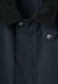 Mørk marineblå frakke med sort fløjlsagtig krave, med metalliske trykknapper mærket med brandnavn.