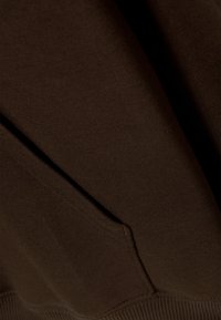 Felpa marrone con una texture morbida e orlo a coste. Presenta una tasca frontale con un sottile dettaglio di cucitura.