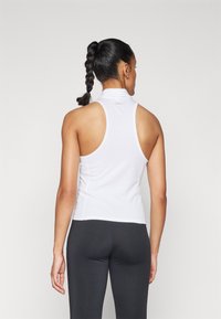 Top atletico bianco senza maniche con colletto alto e design aderente, realizzato in materiale liscio e elasticizzato, abbinato a leggings neri.
