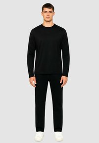 Maglietta nera a maniche lunghe e pantaloni neri, entrambi aderenti, indossati con sneaker bianche. Design semplice senza loghi o motivi visibili.